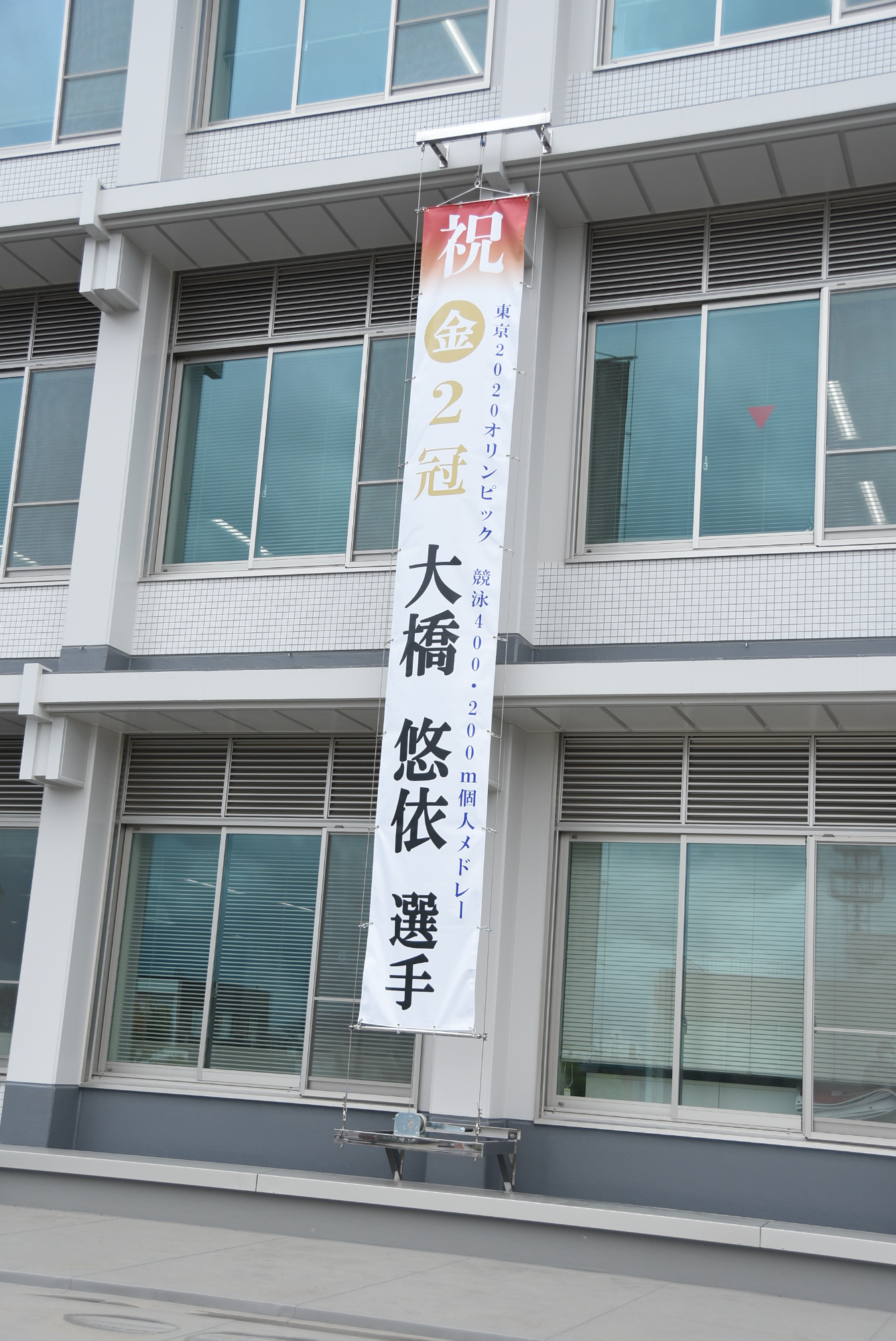 市役所庁舎の外壁に掲出された懸垂幕写真「祝金2冠大橋悠依選手」