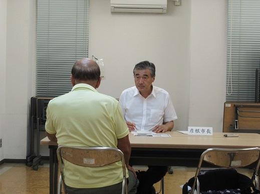 黄色い服を着た高齢男性と対話している市長の写真