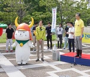 開会式で市長がステージにて挨拶をしている横で担当者の人とならんでいるひこにゃんの写真