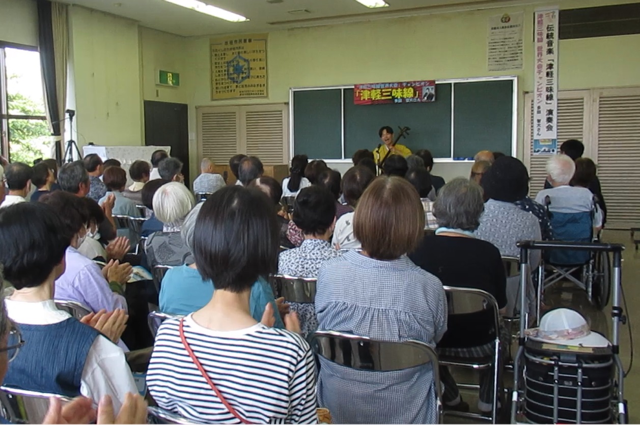 津軽三味線を演奏する男性と歌に合わせて手拍子をする観客