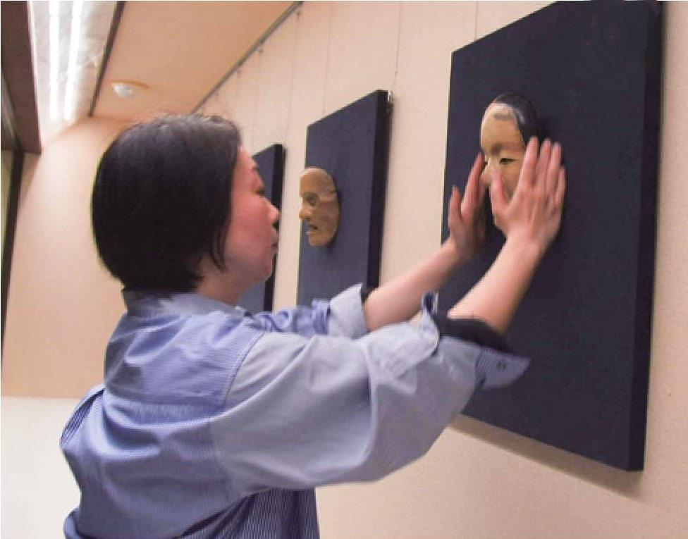 壁に展示された能面に手をかける茨木さんの写真