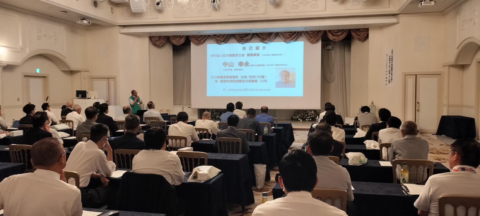 前方にスクリーンがある会場で講師が話し参加者たちが聞いている様子