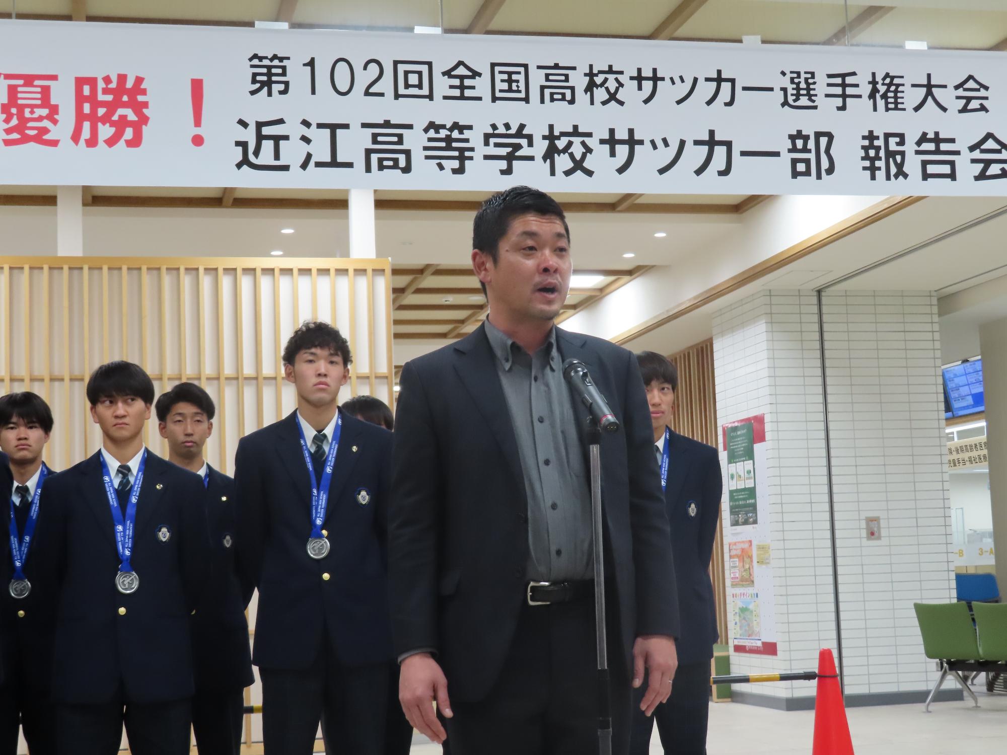 前田監督がマイクの前で報告している様子