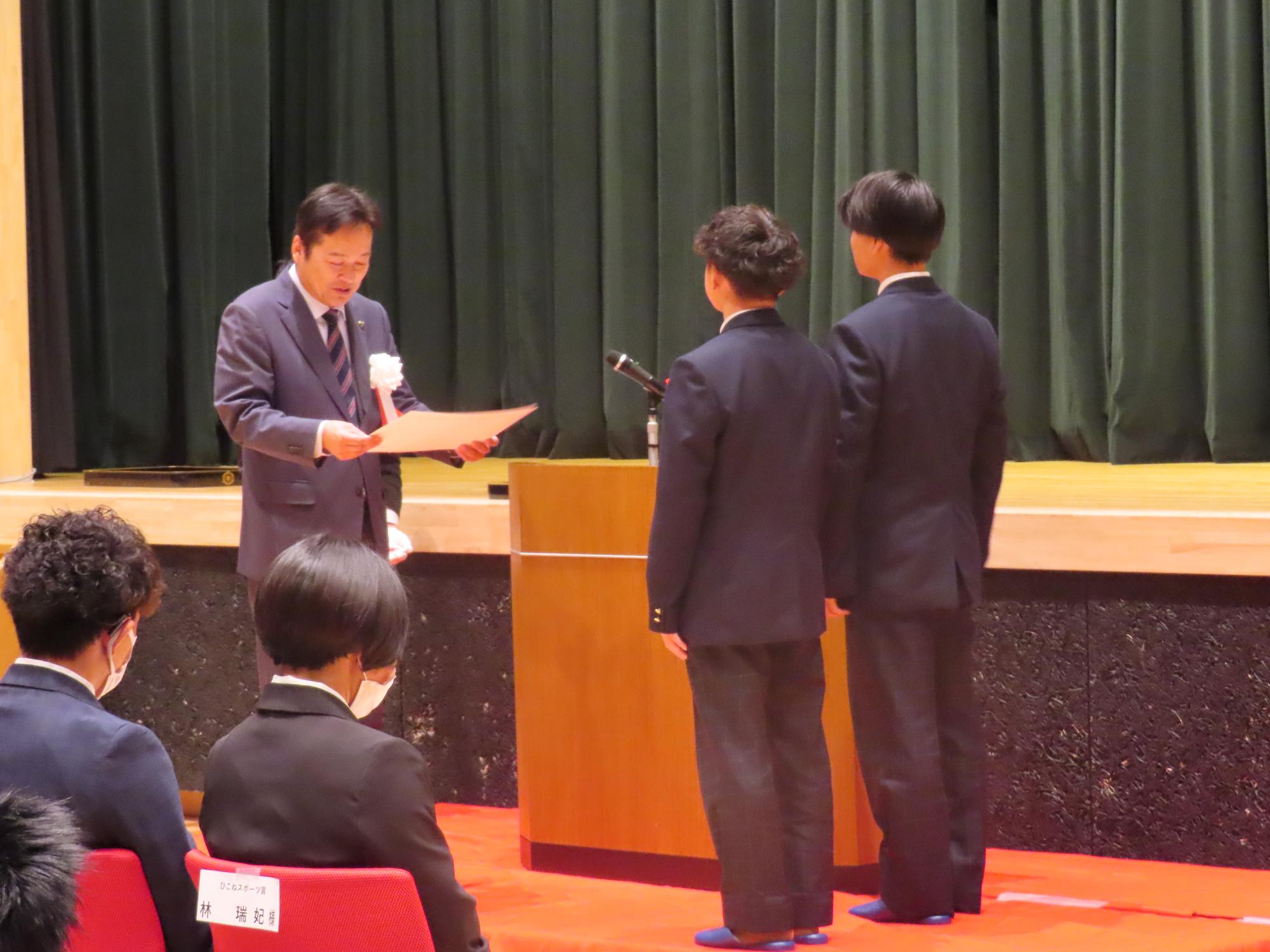 表彰状を読む市長と、前に立つ男性二人
