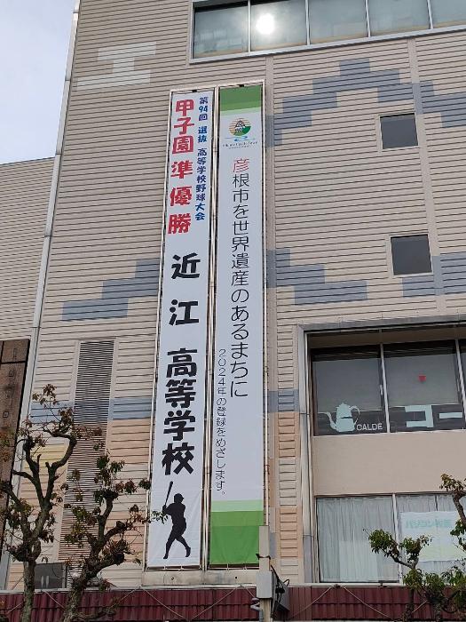 写真（アルプラザ彦根の壁面に「甲子園優勝近江高等学校」の横断幕と「彦根市を世界遺産のあるまちに」の横断幕が並んで掲出されている）