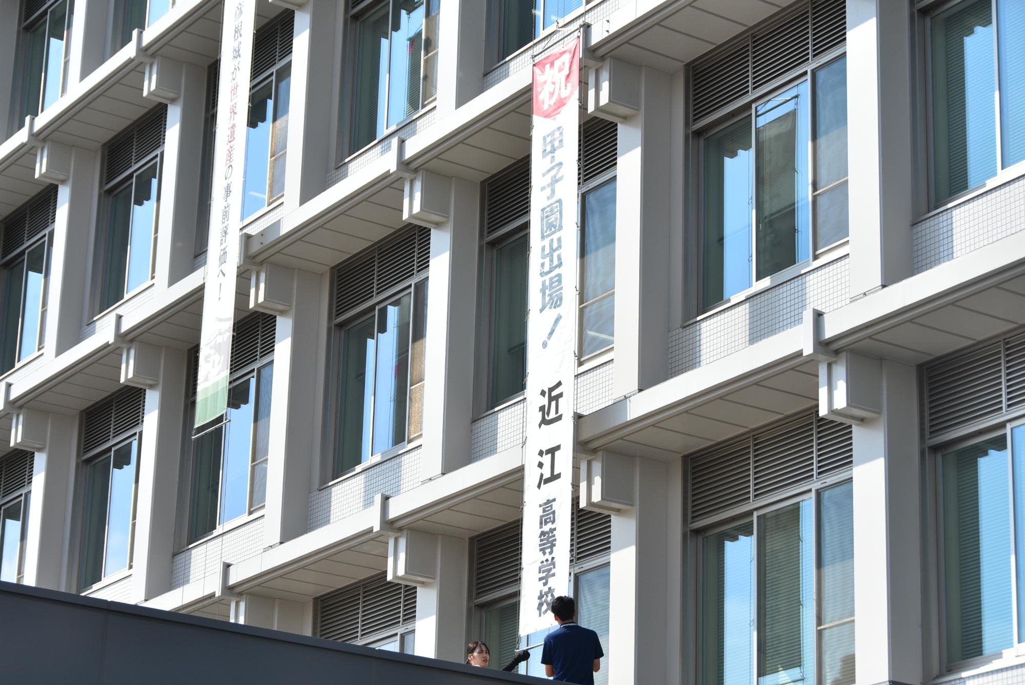 職員が市役所本庁舎の壁に懸垂幕を掲出している様子の写真