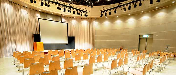 メッセホールの画像（大きなスクリーンと並べられた椅子）