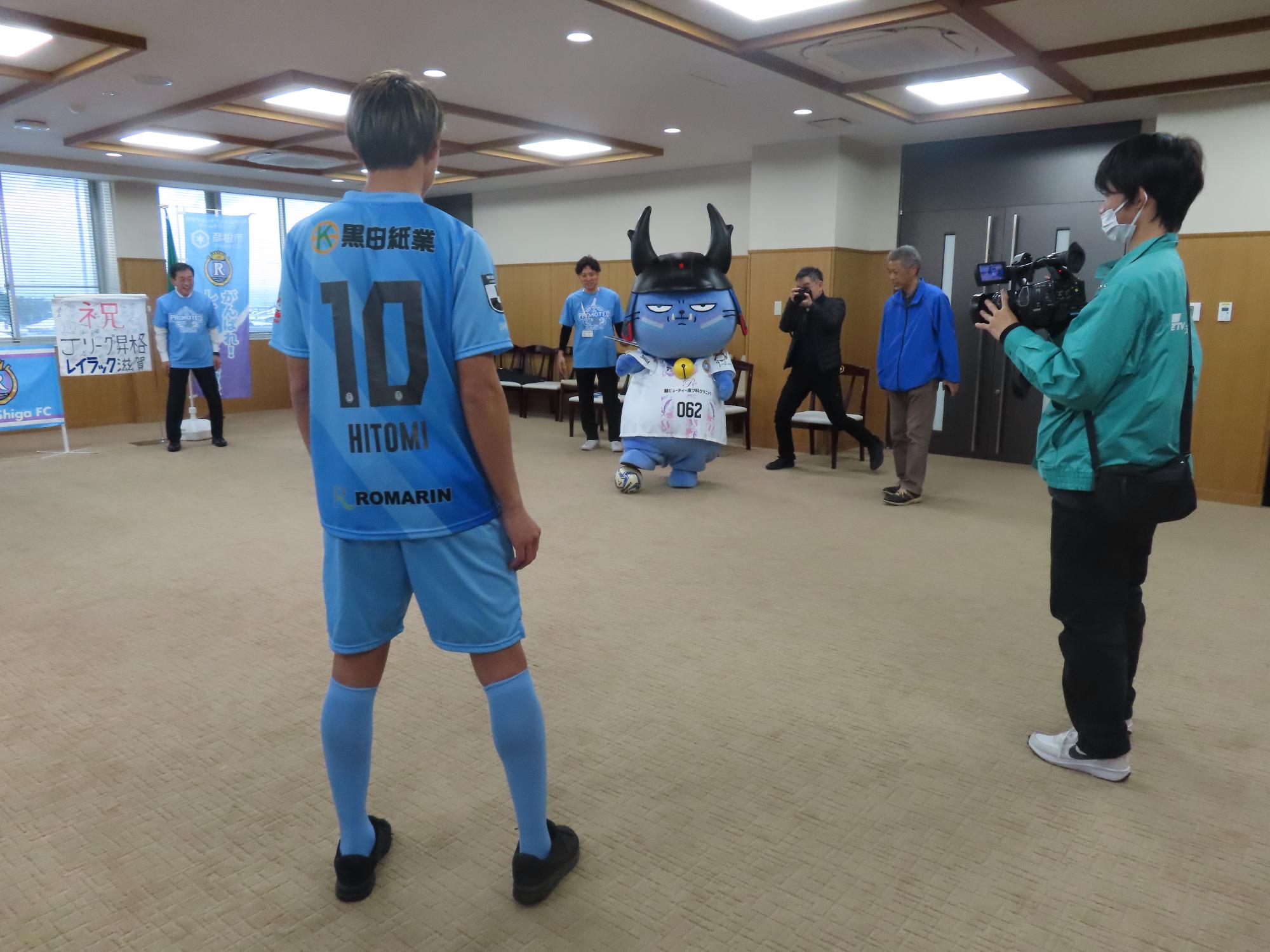 わるにゃんこ将軍が選手と向かい合い、ボールに足を載せている様子の写真