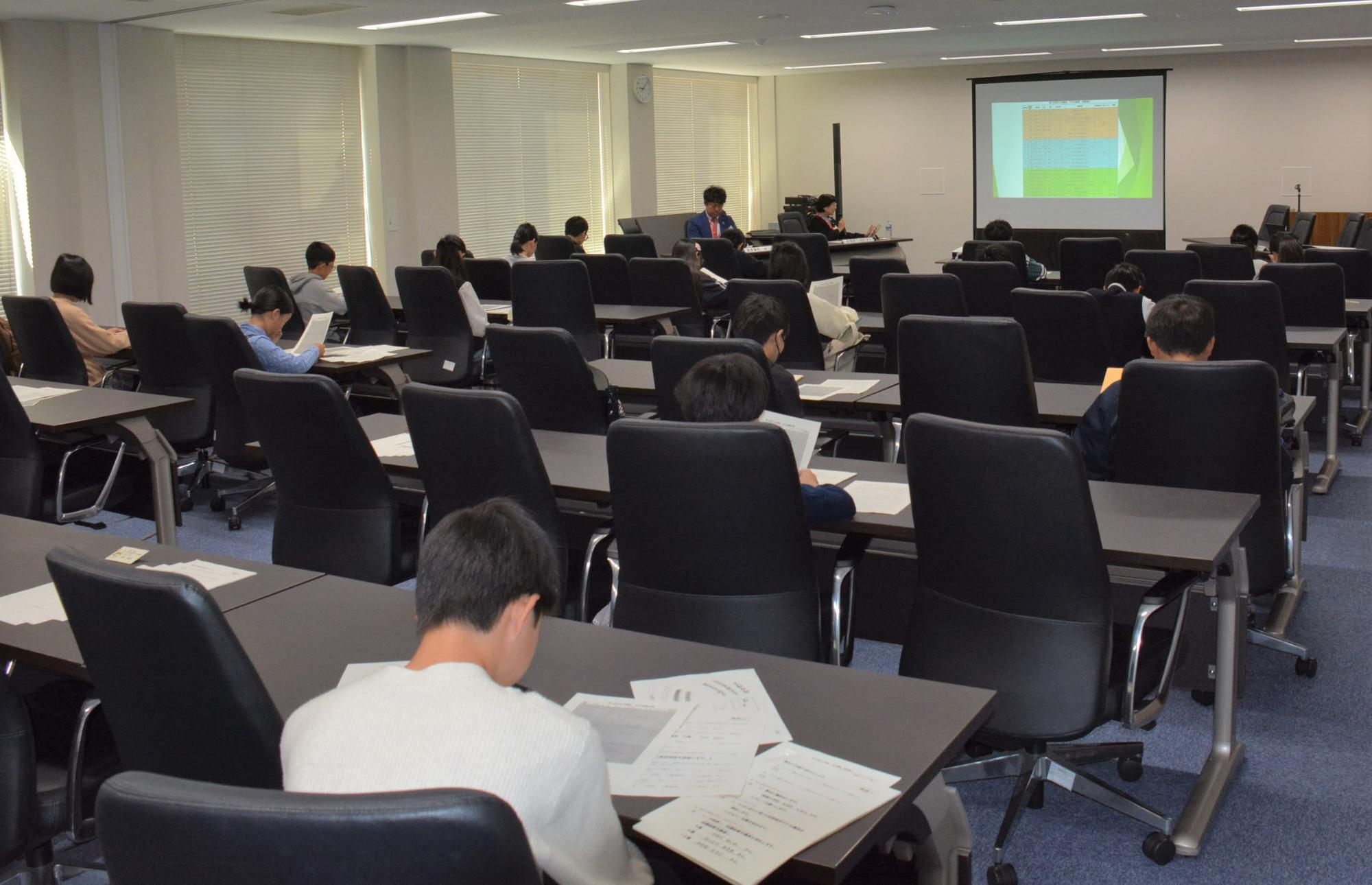 会議室で前方スクリーンや手元の資料を見る子どもたち画像