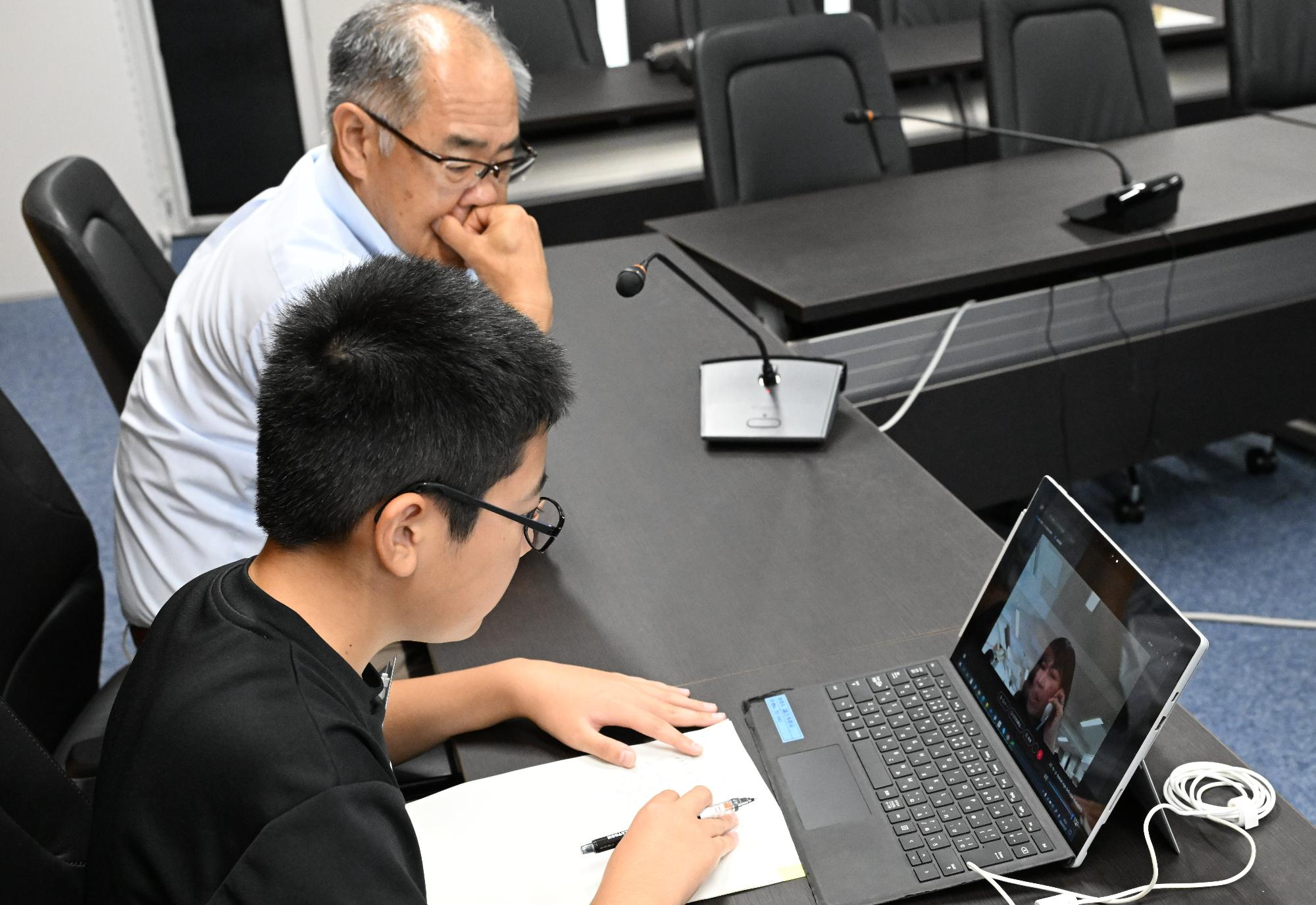手元の書類を見ながら、タブレットのビデオ通話を聞く子供議員の写真