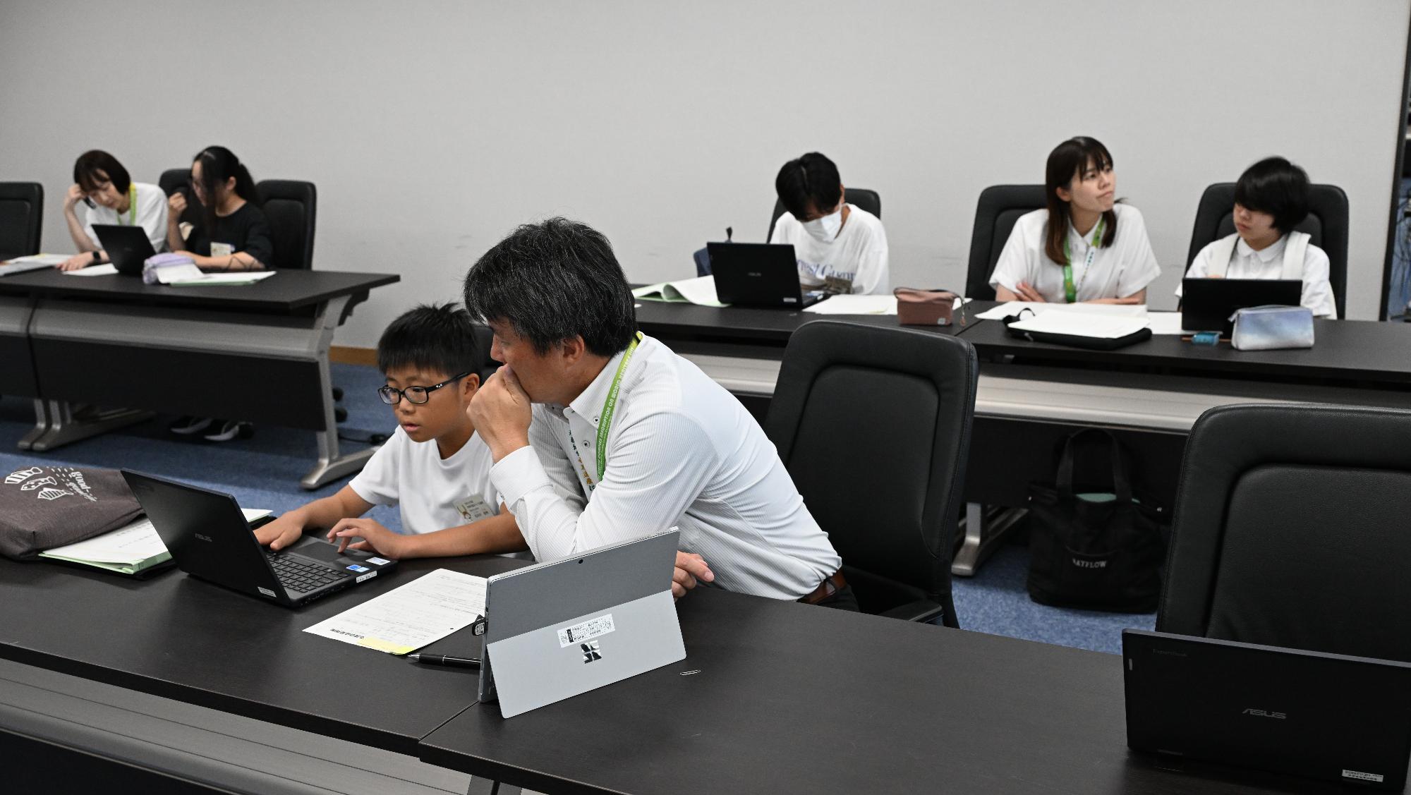 書類をさくせいする子どもと書類を確認する大人の写真