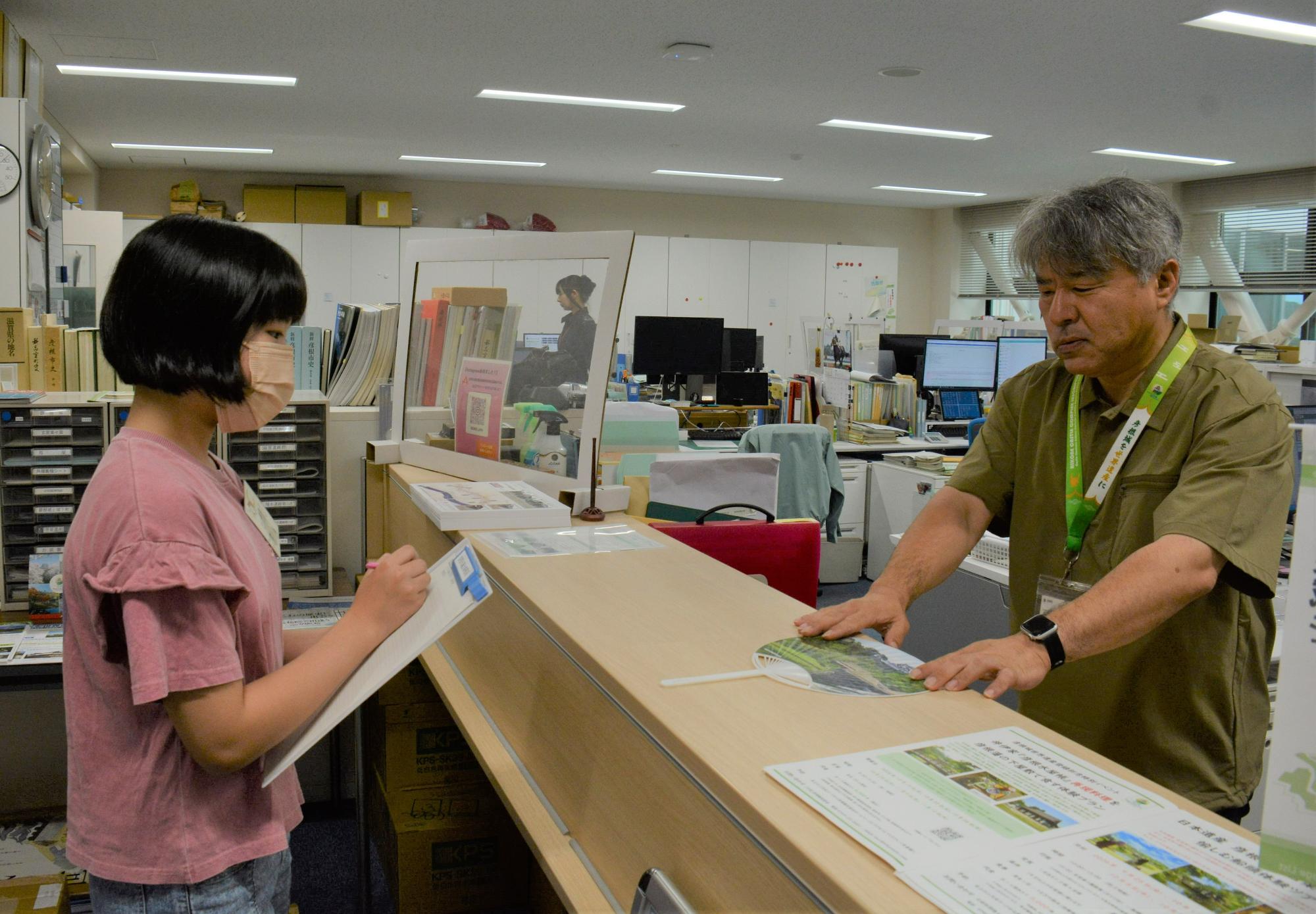 タブレットを使用し説明する職員と、のぞき込む子供議員の写真