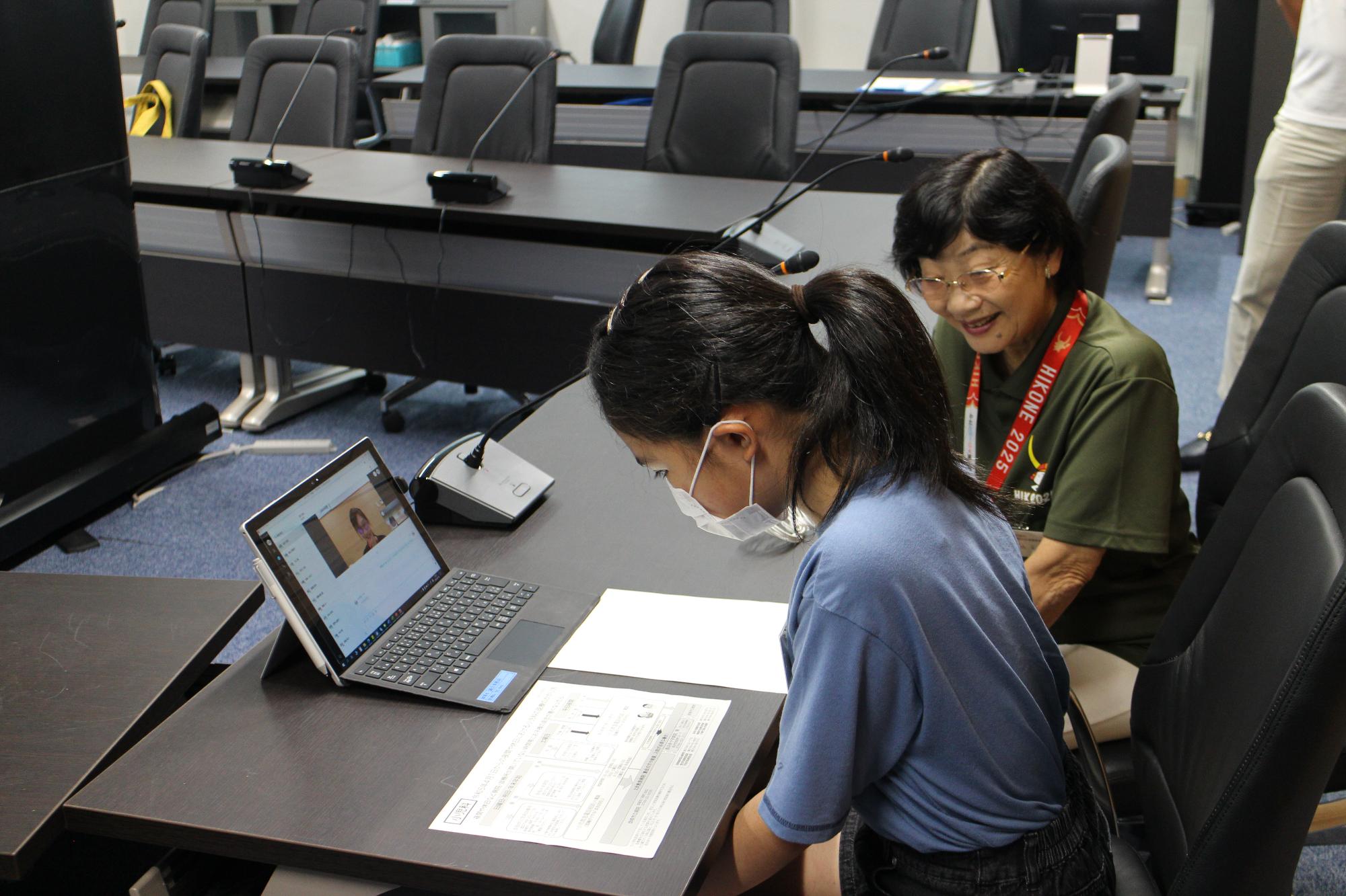 手元の書類を見ながら、タブレットのビデオ通話を聞く子供議員の写真