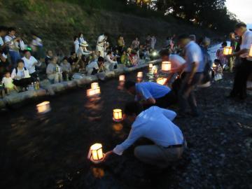 赤く灯った万灯を川に流している人々の写真