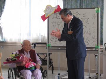 男性最高齢者の「尾本捨三」さんに花束を渡しお祝いしている市長の写真