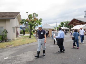 作業着に帽子をかぶりかすみ会まつりに参加してさっとうと歩いている市長の写真