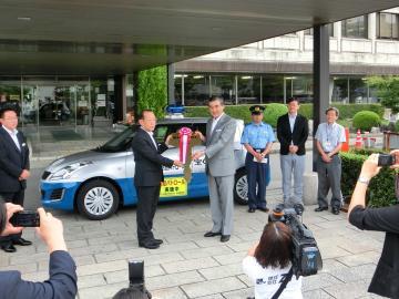 防犯パトロール車の前で大きなカギを持って記念撮影をしている写真