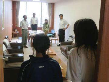 部屋の奥に幹部会議出席者4名、手前に女子中学生2名が挨拶している写真