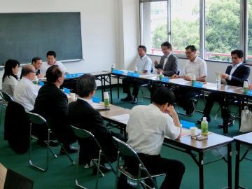 長方形に並べた机を囲んで会議を行っている様子の写真