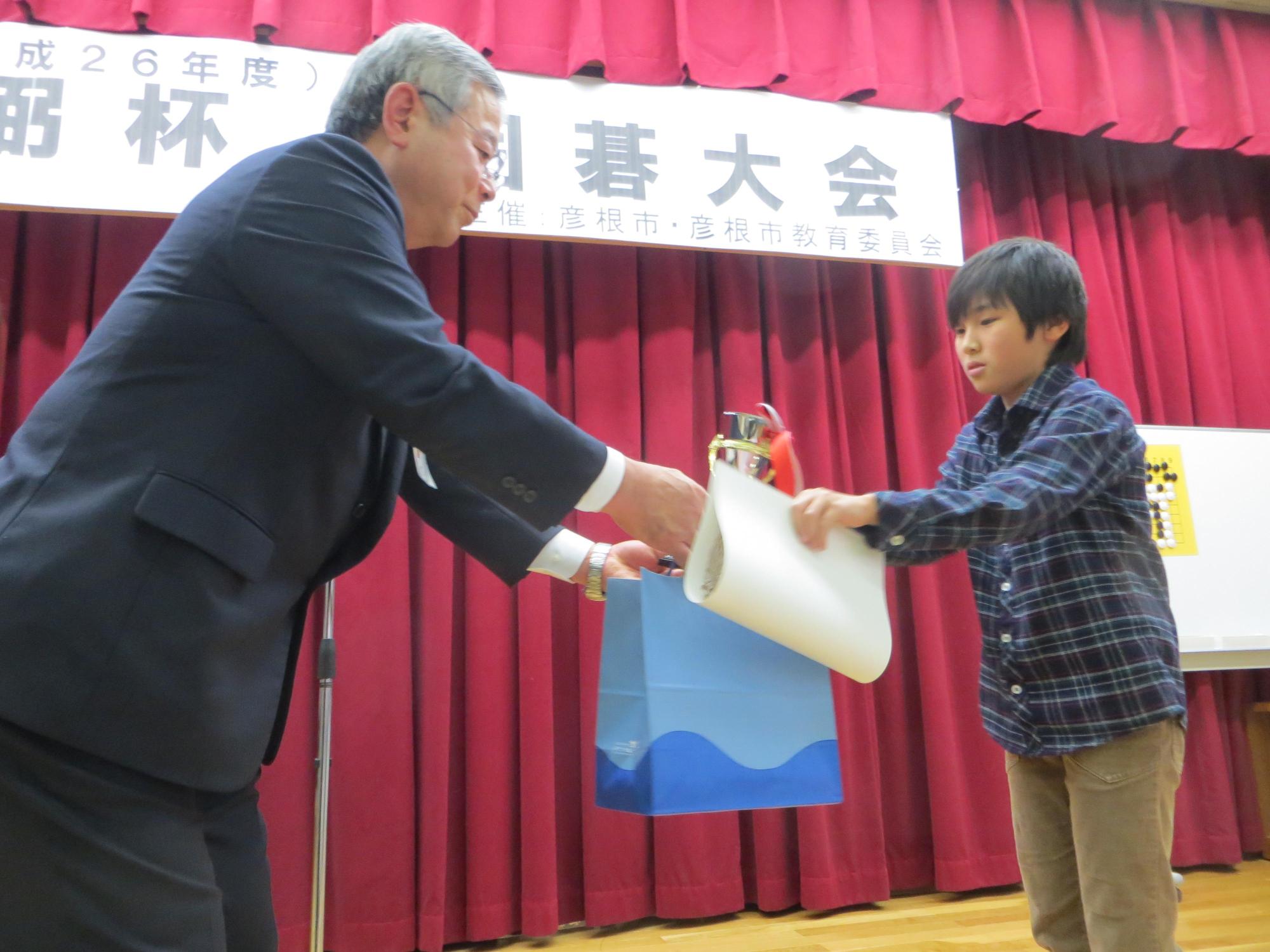 懸賞詰碁で当選者の男児に商品を手渡している様子の写真