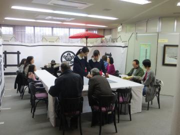 茶道部の生徒二人が9名の来場者にお茶をふるまっているの写真