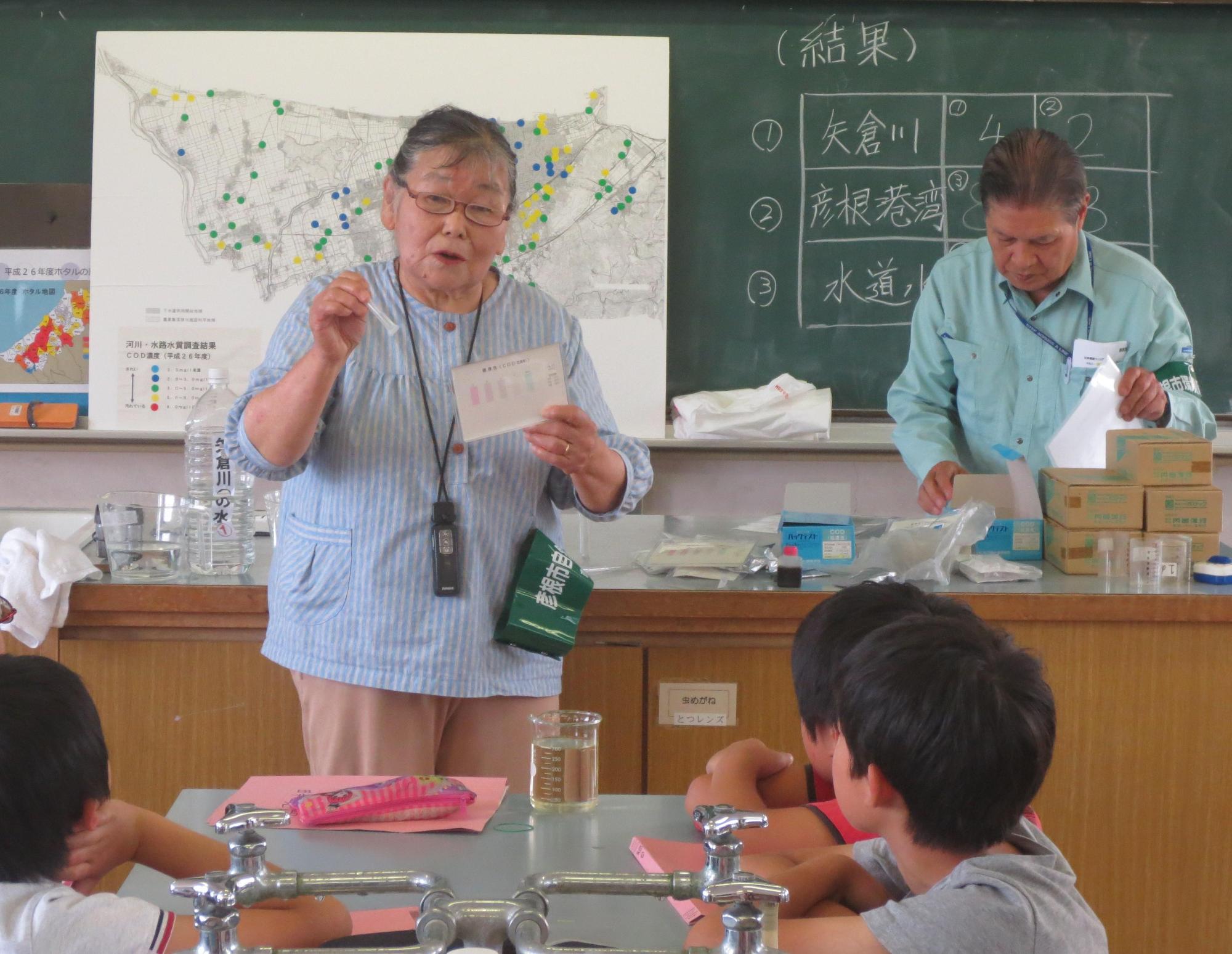 水質分析結果を説明する指導員とそれを聞いている生徒の写真