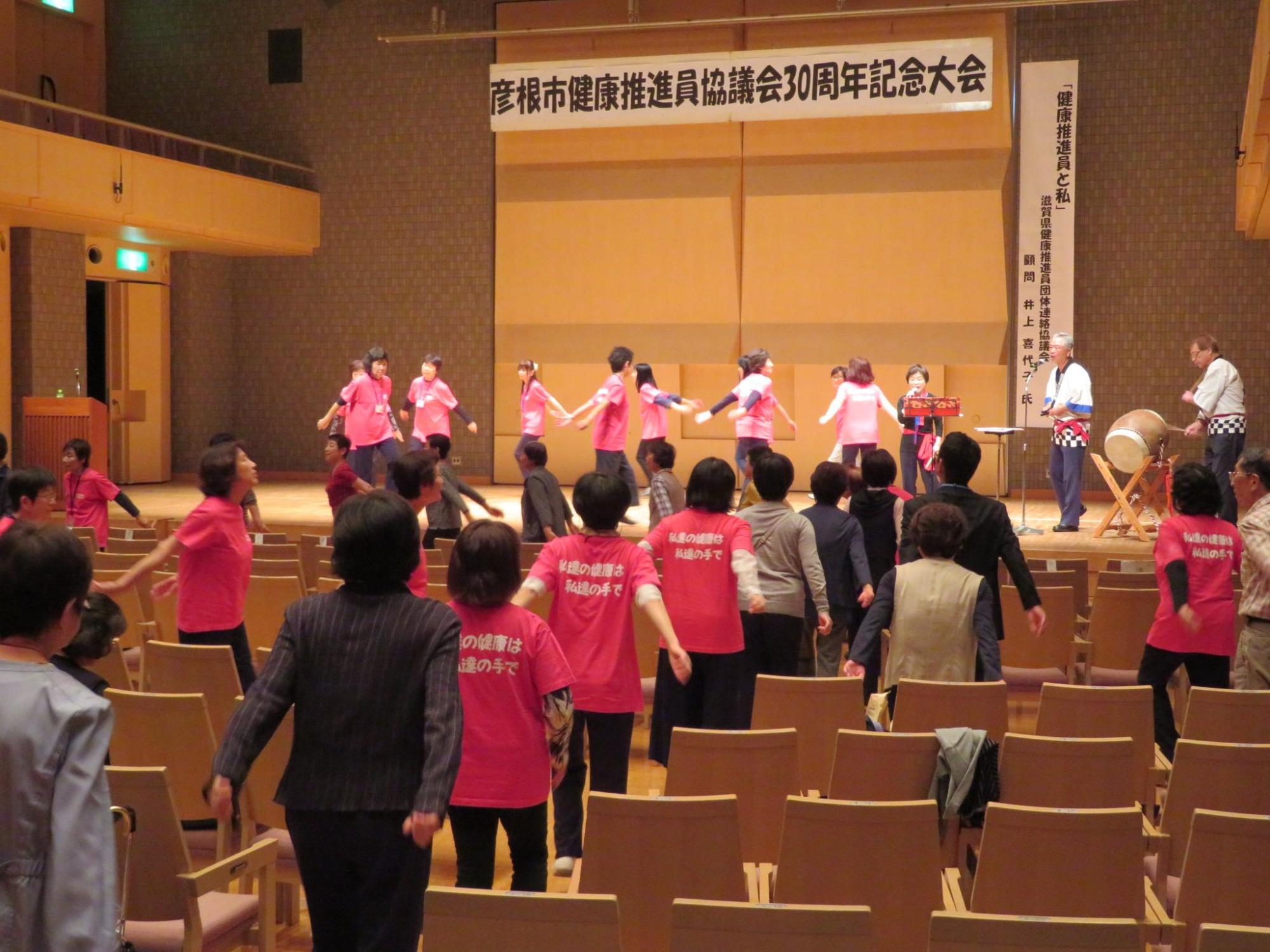 今大会の参加者が輪になって、壇上と客席の通路を使って江州音頭を踊っている写真