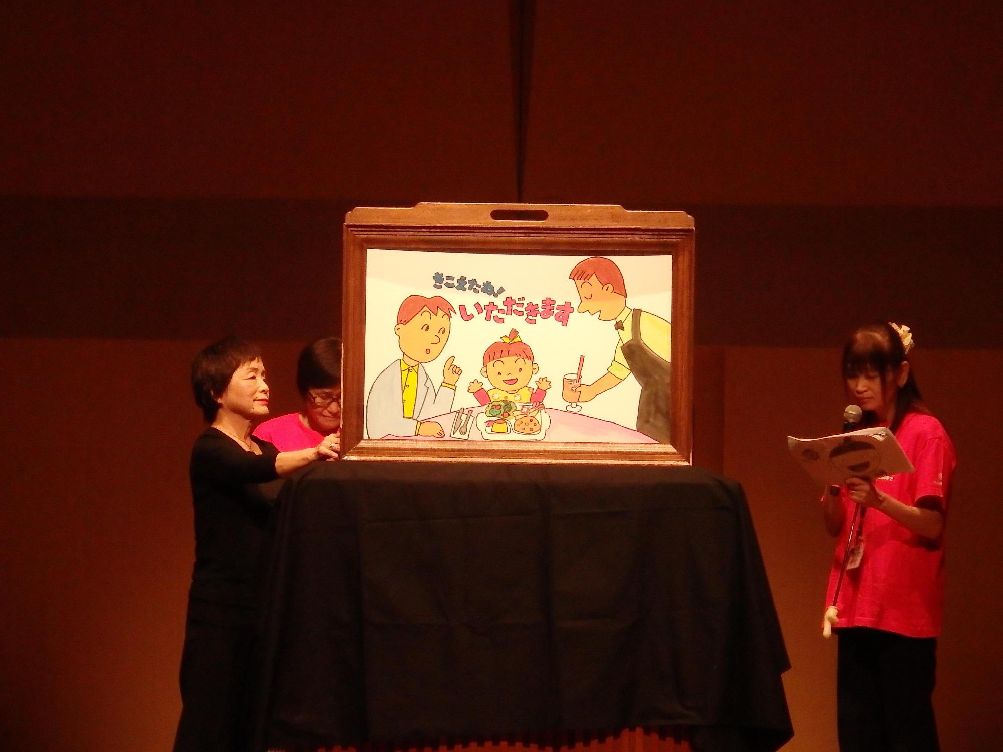 壇上にて3名の女性が食育に関する紙芝居を披露している写真