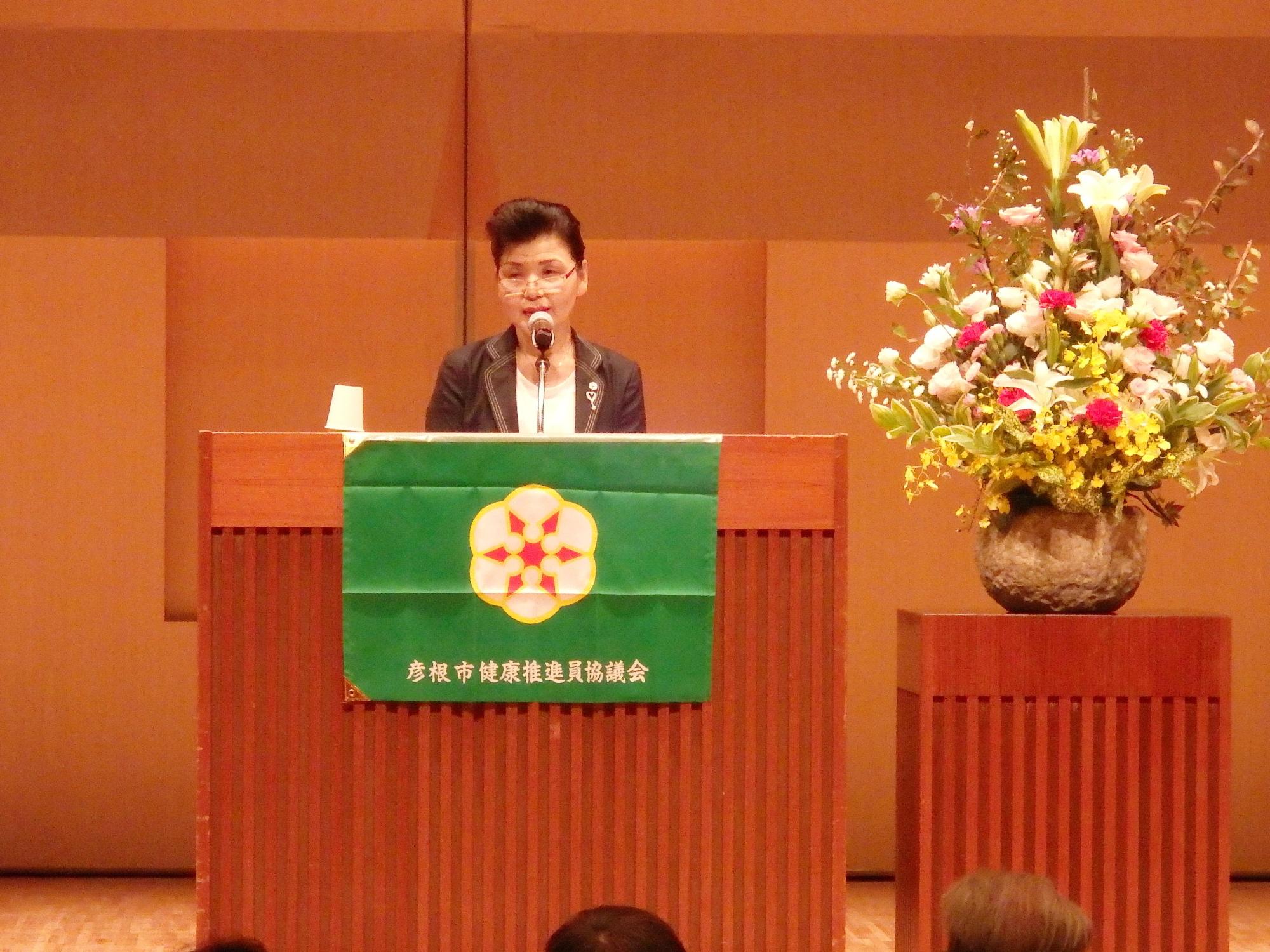 壇上にて、滋賀県健康推進員団体連絡協議会の顧問である井上喜代子様が「健康推進員と私」と題した講演を行っている写真