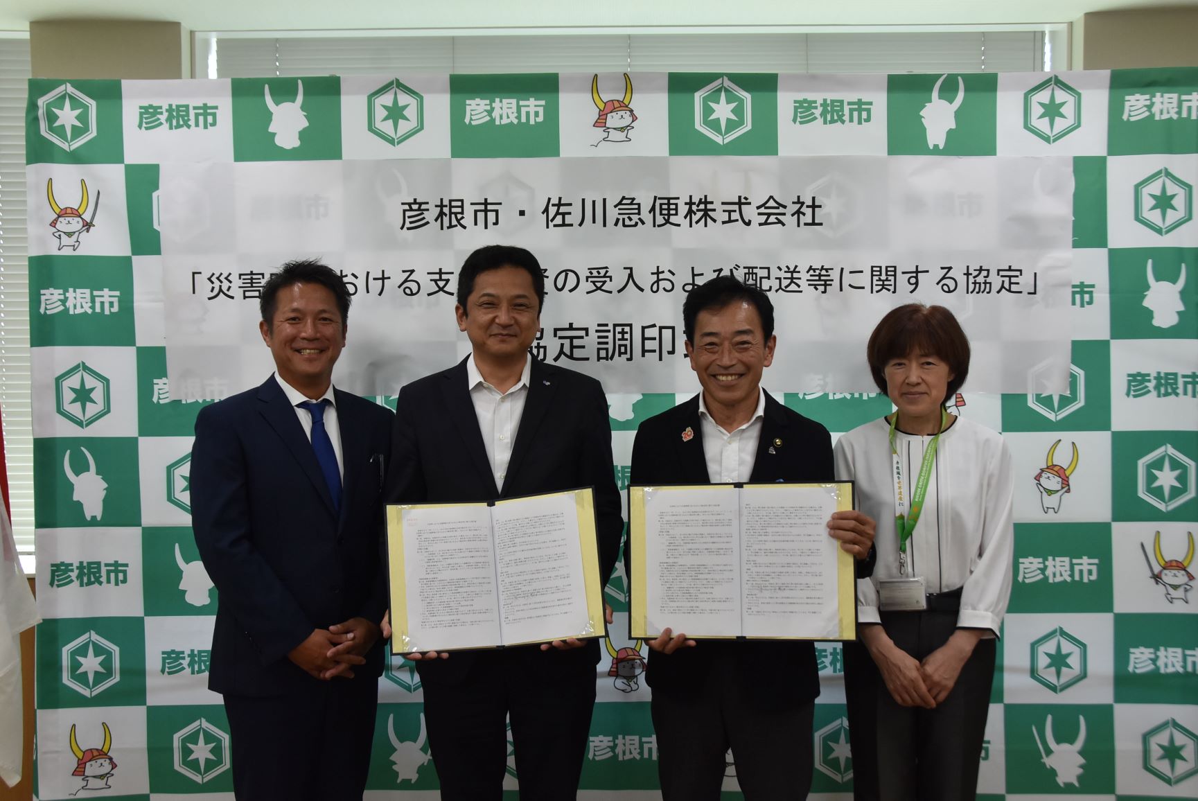 調印式と書かれた幕の前で、協定書を広げて記念撮影