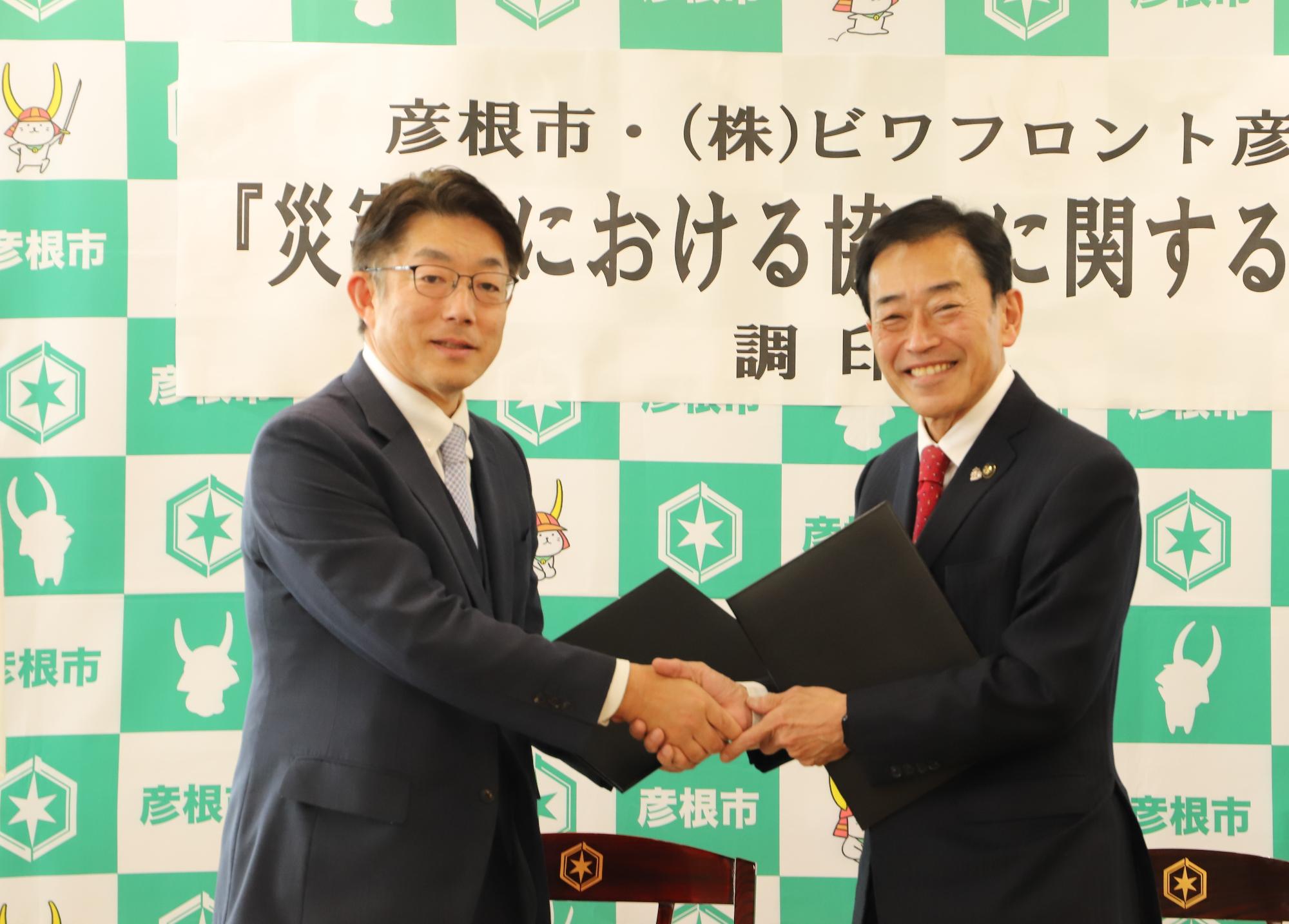 協定書を手に握手する市長と木下氏の写真