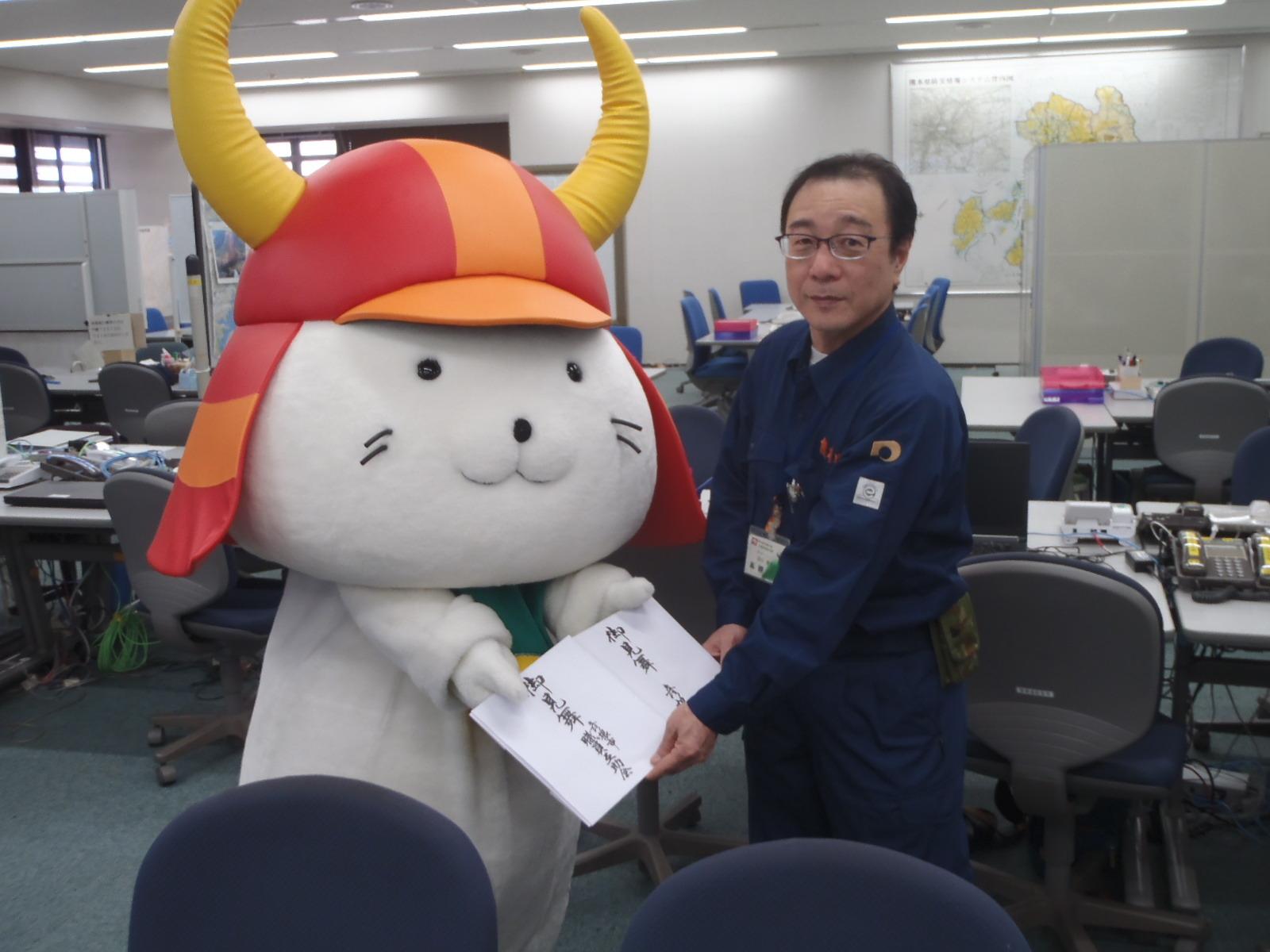 災害見舞金目録謹呈の際ひこにゃんと熊本県知事公室危機管理防災課長が正面を見ている写真