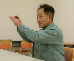 椅子に座って身振りしながら話している男性の写真