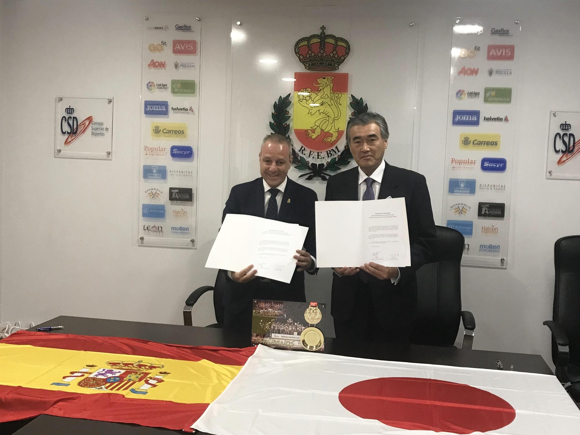 日本とスペインの国旗を机に飾り締結した合宿の覚書を手にもちならんでいる大久保市長と県・市の担当者と王立スペインハンドボール連盟フランシスコ・ブラスケス会長の写真