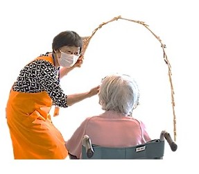車椅子に座る患者さんの前で南京玉すだれを披露するエプロン姿の女性