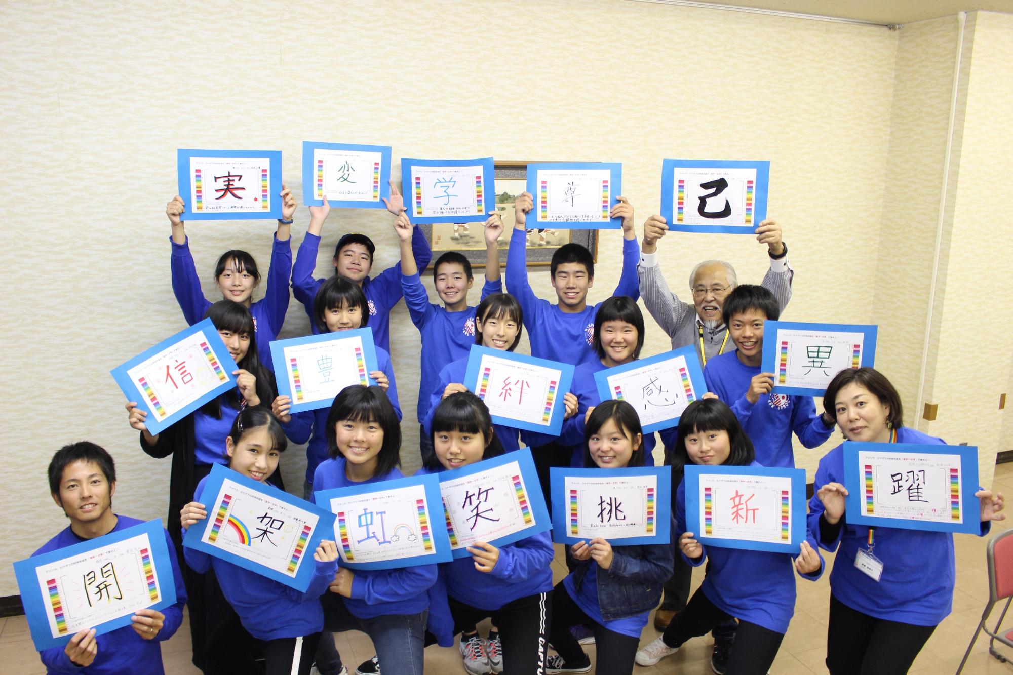 派遣団の人達がおそろいの青いシャツを着て今回の研修を漢字一文字で表した用紙を一人一人もち笑顔で撮った集合写真