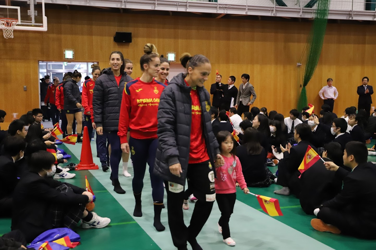 会場に子供と手をつないだ選手が入場してくるのを、高校生たちが旗を持って出迎えている様子