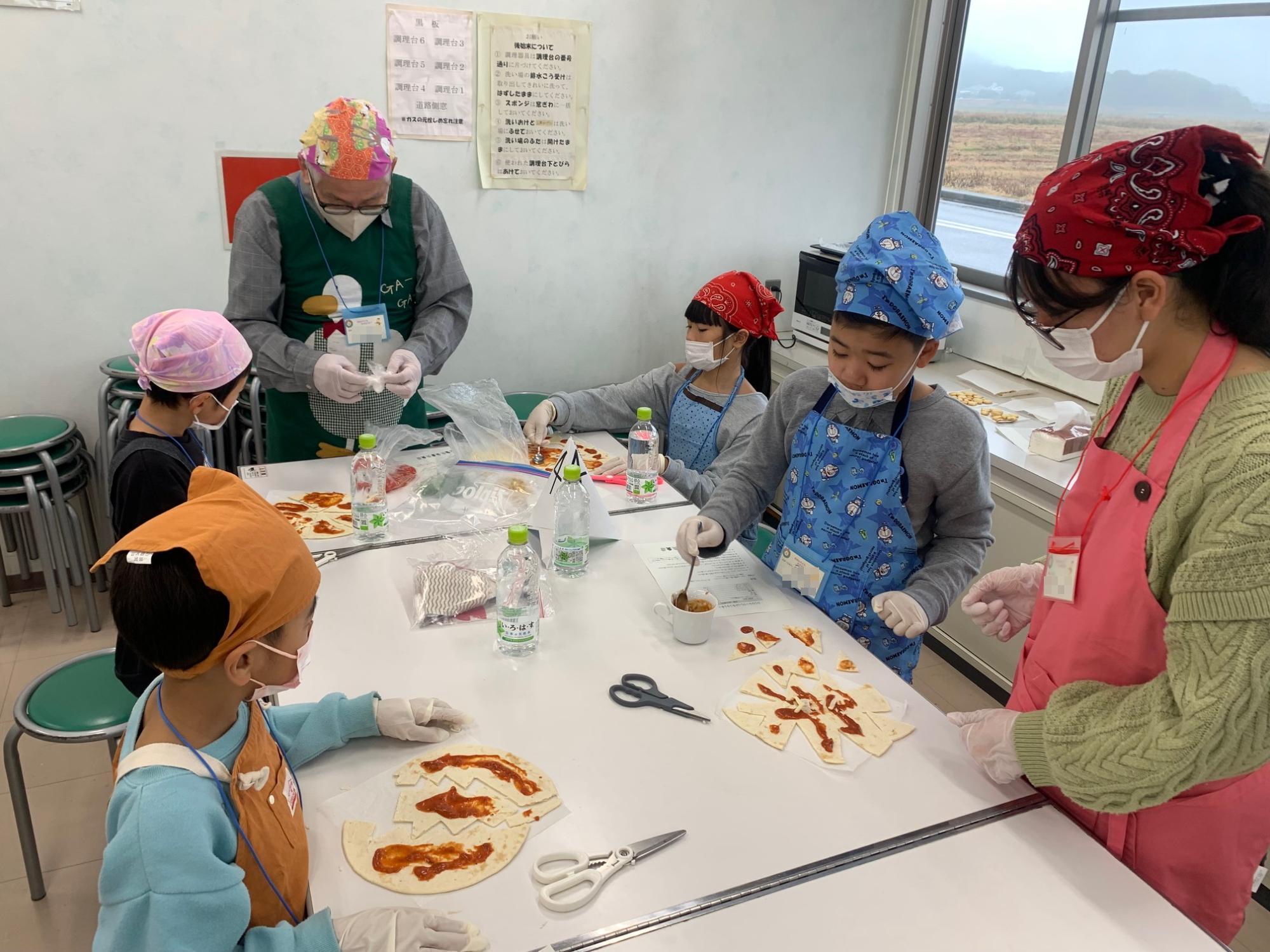 子どもたちが大人に教わりながらピザを作っている様子の写真