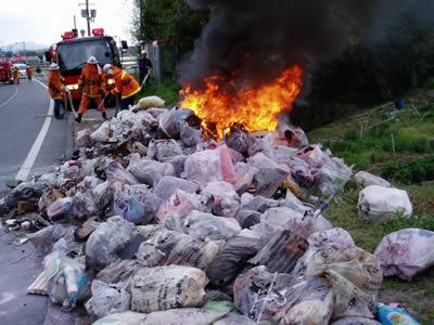 ゴミ収集車から取り出された燃えているゴミを消防隊員が消化している写真