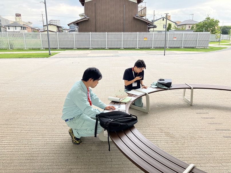 屋外のベンチに書類を置き、確認する職員の様子