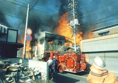 火災のため燃えている家と消防車と消防士の写真